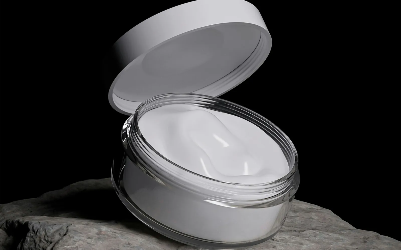 Geöffnete Cremedose aus Kunststoff mit weißer Creme auf einem Stein