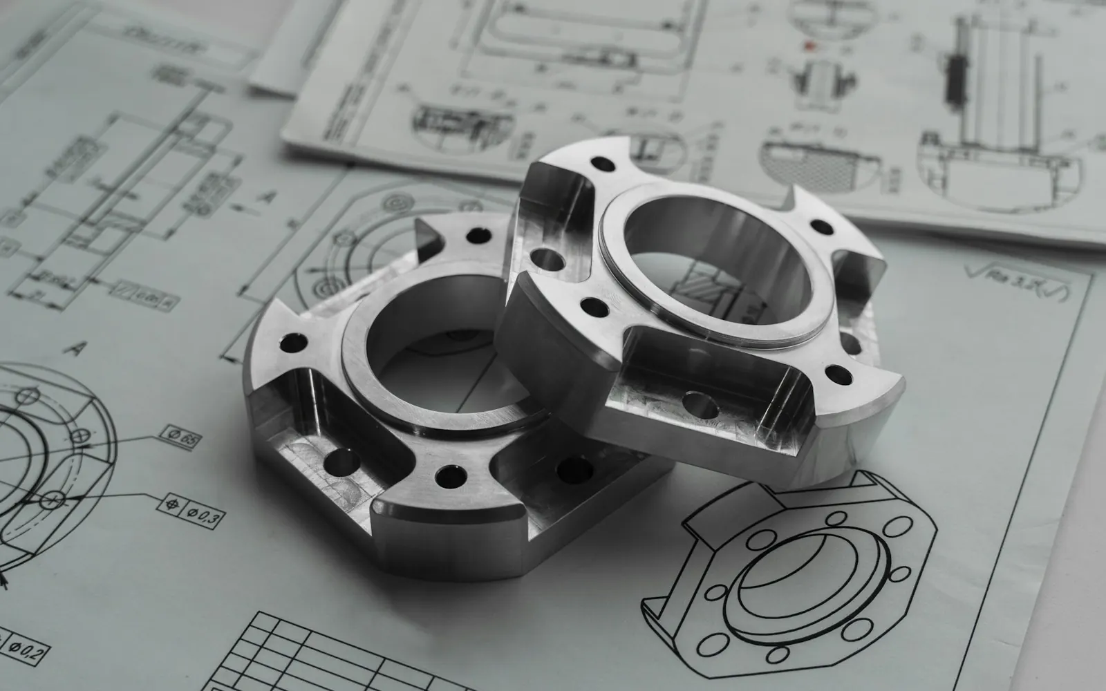 Zwei metallische Maschinenbauteile auf technischen Zeichnungen