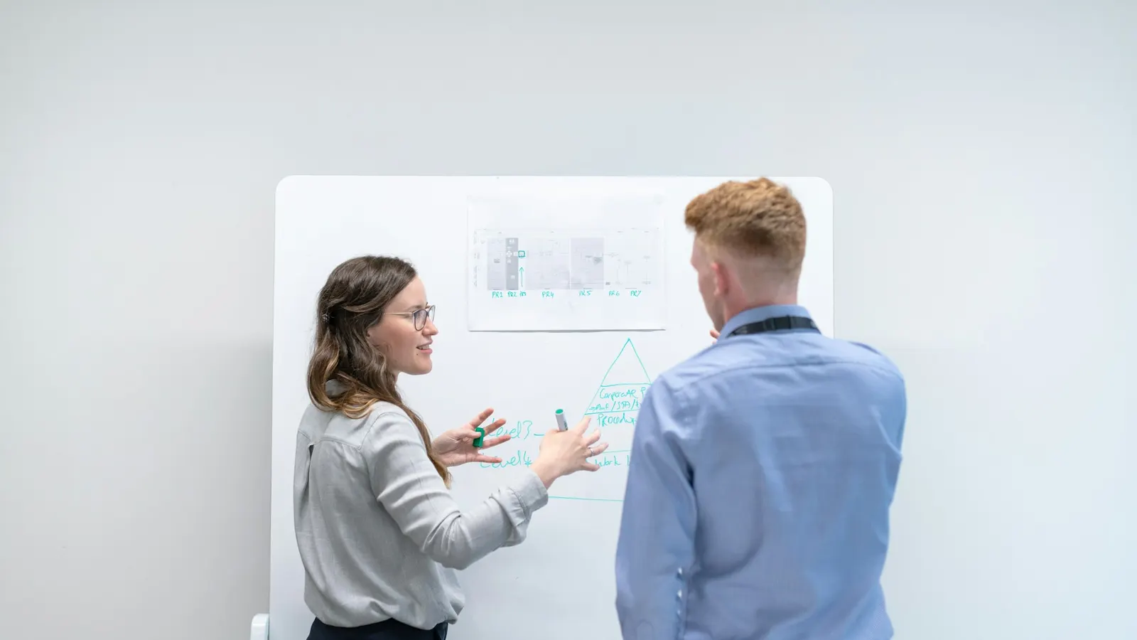 Zwei Kollegen besprechen eine Skizze an einem Whiteboard in einem hellen Büro