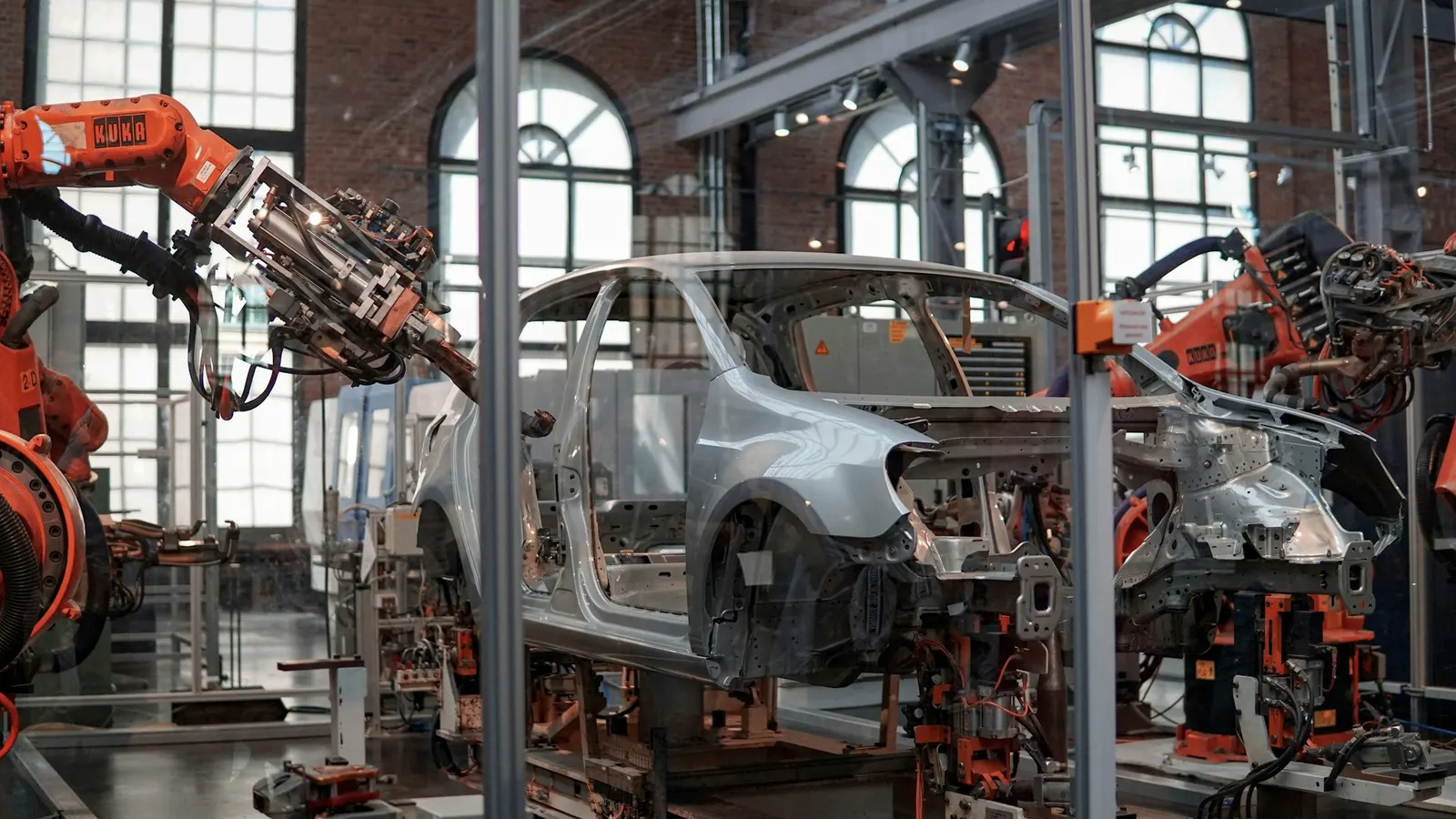 Roboterarme in einer hellen Montagehalle bearbeiten eine Fahrzeugkarosserie