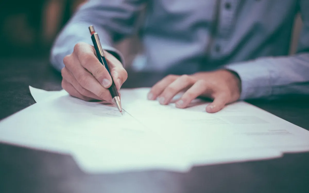 Hand mit Stift über Vertragsunterlagen auf einem Schreibtisch
