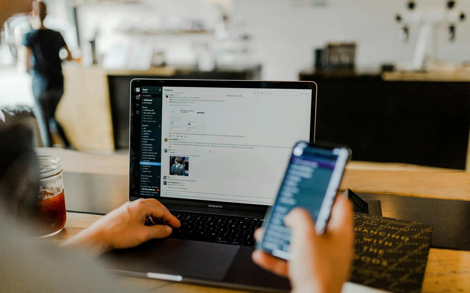 Person arbeitet am Laptop und schreibt parallel eine Nachricht auf dem Smartphone