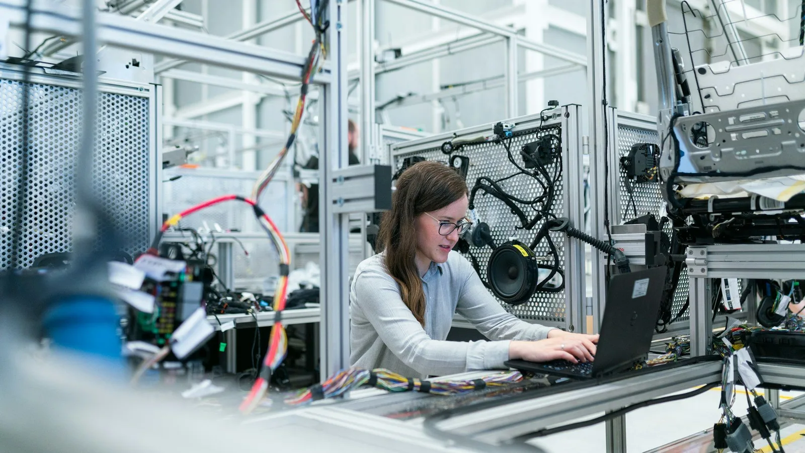Mitarbeiterin arbeitet am Laptop in einer Fertigungs- und Prüfumgebung